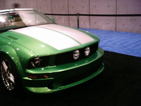 1986 Ford Bronco - A green convertible car with white racing stripes is displayed indoors.