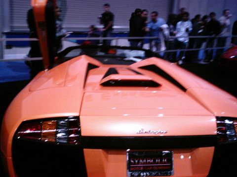 1986 Ford Bronco - Orange Lamborghini sports car with doors open, seen at an indoor event.