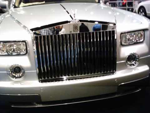 1986 Ford Bronco - Head-on close-up of a silver Rolls-Royce Phantom on an indoor show floor, centered on the tall chrome Pantheon grille with the RR badge and…