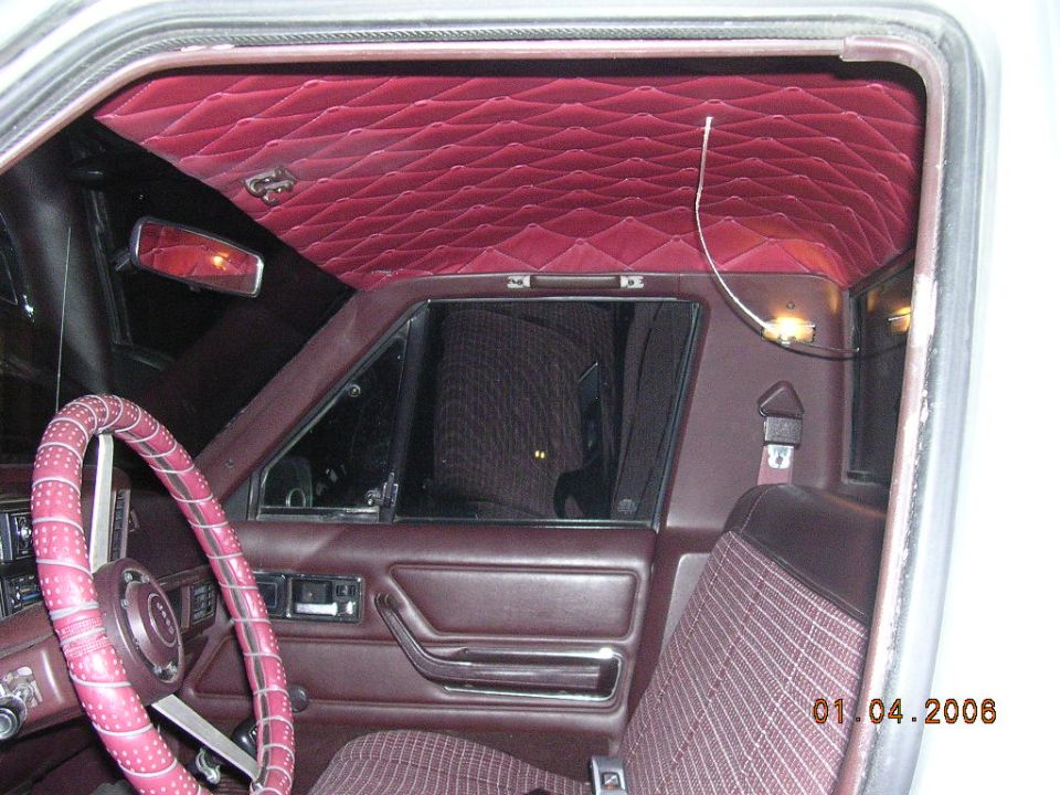Jeep Cherokee interior with diamond-stitched red headliner, maroon door panels, and patterned seat fabric. A pink steering wheel cover is visible