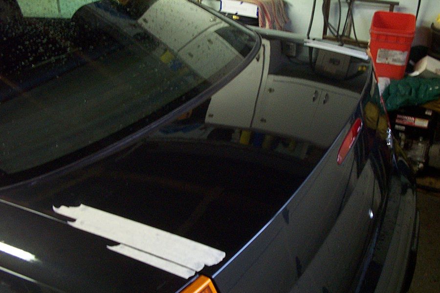 Masking tape strips marking spoiler placement on the trunk lid of a dark sedan