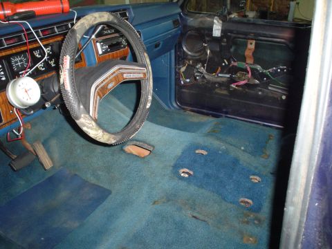 1984 Ford Bronco - The interior of a vehicle shows worn blue carpet and exposed wiring in the door panel.