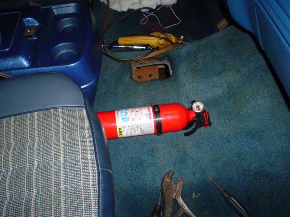 Vehicle interior with blue seats, a red fire extinguisher, and tools on the teal carpet