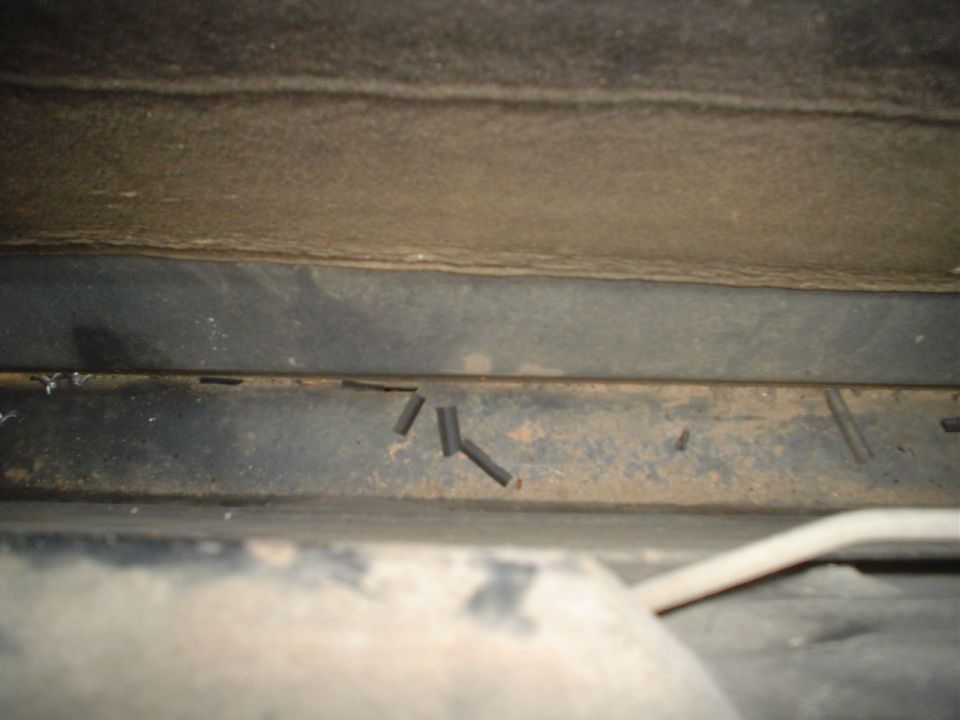 Close-up of the underside of a vehicle, showing some metal framing and what appear to be cut wires or tubes