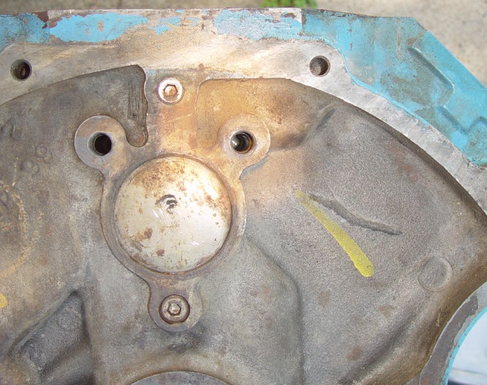 Rear face of a bare engine block showing core plug, bolt holes and traces of blue paint