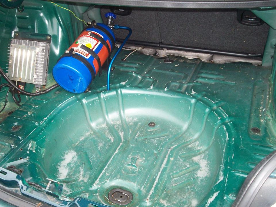 Bare green trunk floor with spare tire well, mounted blue nitrous bottle and finned amplifier with wiring