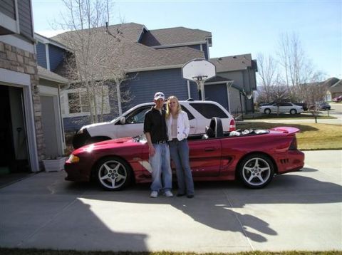 1996 Ford Probe - A red convertible sports car is parked in a driveway with a white SUV behind it and two people standing next to the car.
