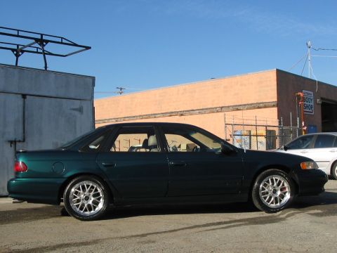 1995 Ford Taurus - Dark green 1995 Ford Taurus SHO seen from the side, parked near a body shop.