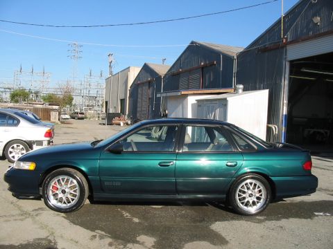 1995 Ford Taurus - A green sedan is parked in front of some warehouses under a clear blue sky.