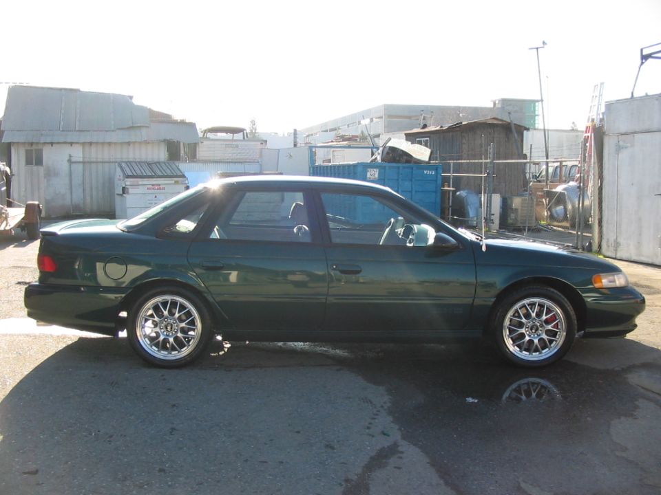 1995 Ford Taurus sedan, side view, dark green paint, aftermarket wheels