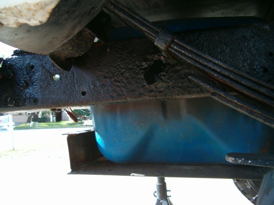 Undercarriage view of a vehicle, showing a blue fuel tank and rusty frame components