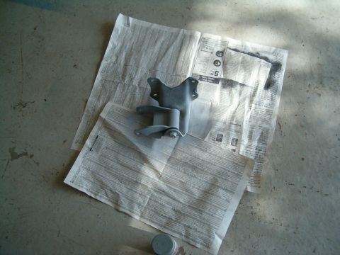 1979 Ford Bronco - A metal bracket, likely a car part, is placed on newspapers for painting.