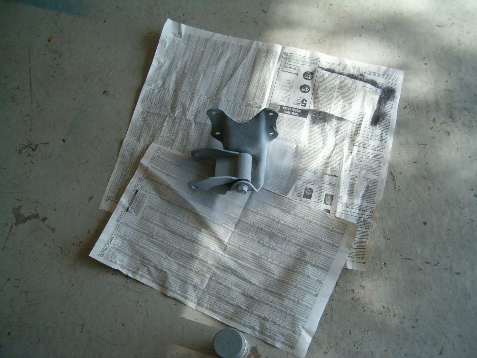 Painted metal bracket resting on newspapers on a concrete floor