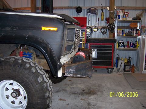 1985 Ford Bronco - The front end of a modified truck is shown in a garage with tools and shelves in the background.