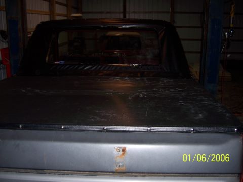 1985 Ford Bronco - Rear view of a gray Ford Bronco with a black soft top and bed cover, parked indoors.