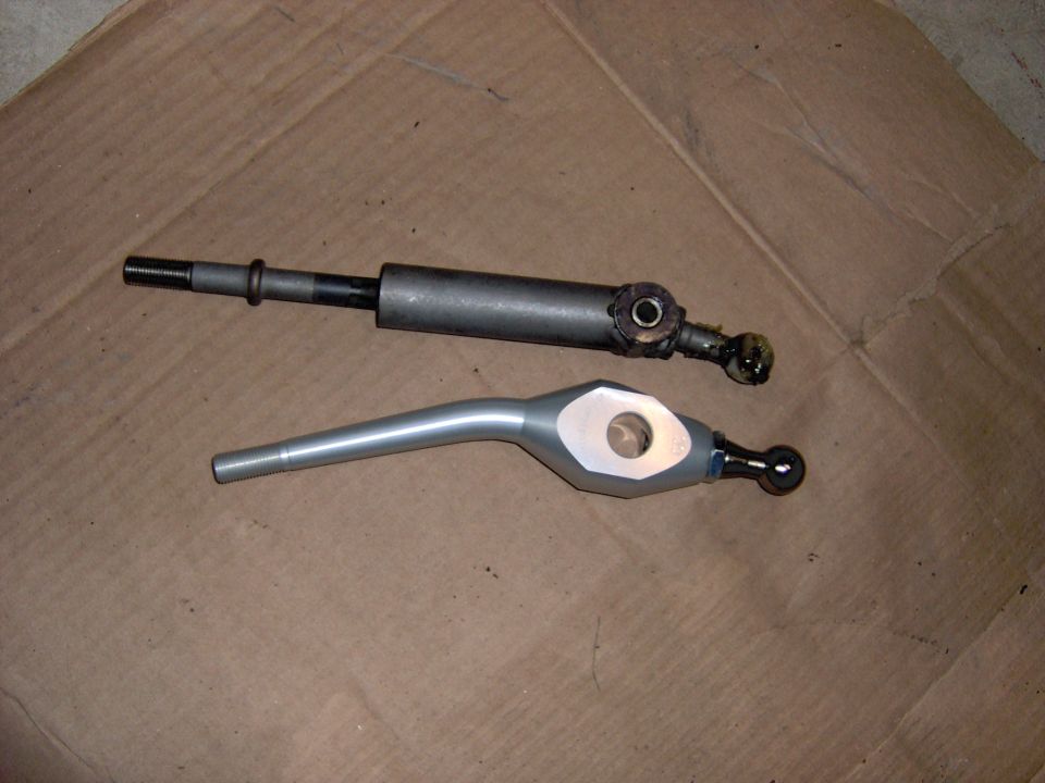 Stock black shifter rod next to new silver aluminum short-throw shifter on cardboard