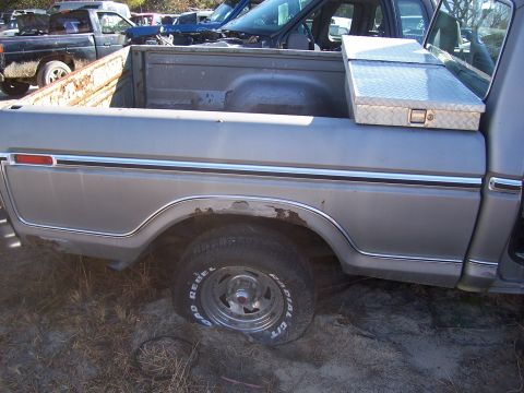 1978 Ford Bronco - Pickup truck bed and side view, showing rust and a toolbox. Other vehicles are in the background.