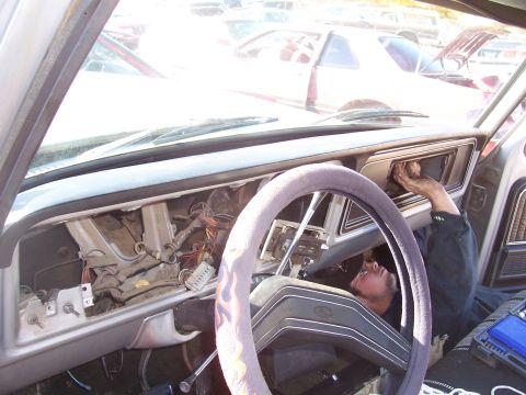 1978 Ford Bronco - A person works on the exposed dashboard of a 1978 Ford Bronco, with other vehicles visible in the background.