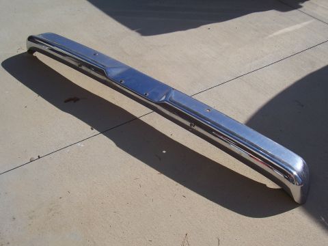 1978 Ford Bronco - A chrome bumper lies on a concrete surface, casting a long shadow.