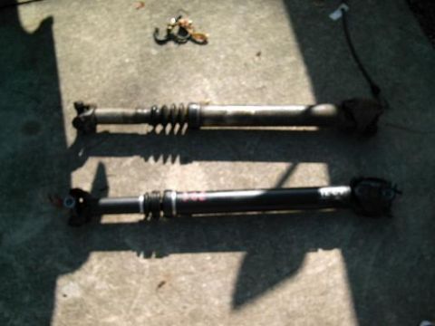 1986 Ford Bronco - Two driveshafts are shown on a concrete surface. One of the driveshafts has red markings on it.