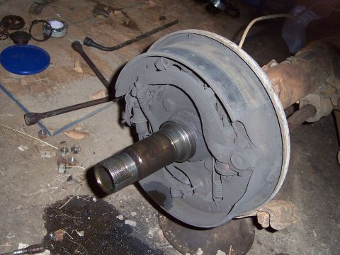 1983 Ford Bronco - Close-up of a rear axle drum brake assembly, with various tools scattered on the concrete floor around it.
