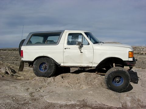 1987 Ford Bronco - A white 1987 Ford Bronco is shown from the side, modified for off-road use on a rocky landscape.
