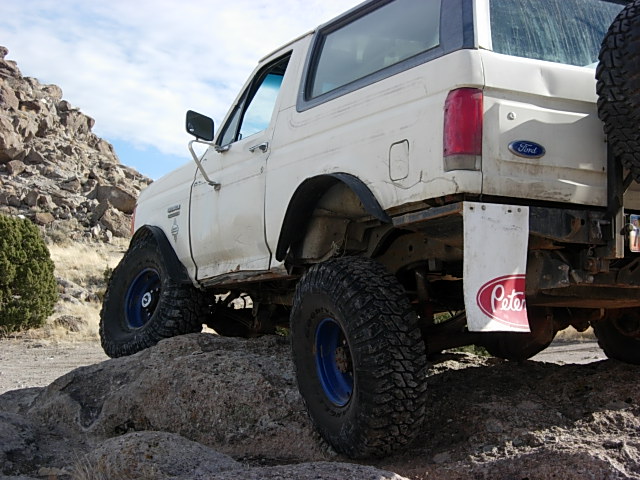 White 1987 Ford Bronco with large tires on rocks, rear view