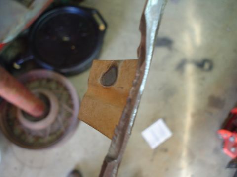 1984 Ford Bronco - A metal bracket with a hole is shown on a floor, with other automotive parts in the background.