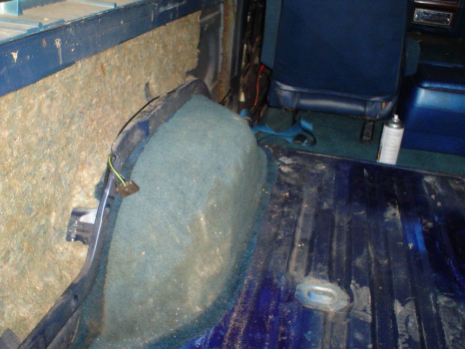 Rear cargo area of a vehicle with blue seats and carpeting. Some insulation is visible on the left wall