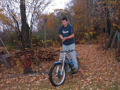 1985 Ford F-150 - A young man stands beside a blue dirt bike in an outdoor setting covered in autumn leaves.