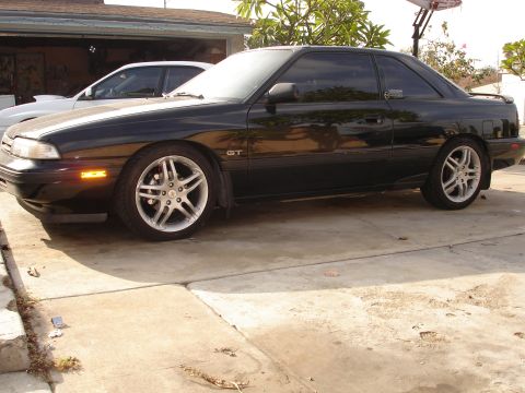 1989 Mazda MX-6 - A black 1989 Mazda MX-6 GT is parked in a driveway next to another vehicle.