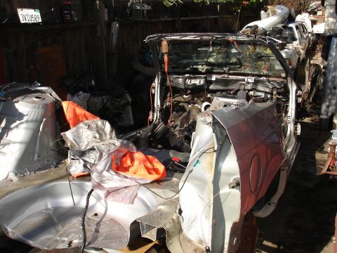 1992 Ford Taurus - A heavily damaged car sits in a junkyard, its interior exposed and parts covered with tarps.