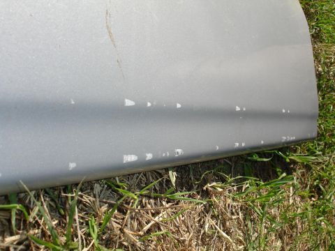 1992 Ford Taurus - The lower edge of a car door shows numerous paint chips, revealing the primer underneath.
