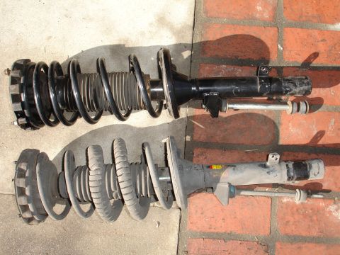 1995 Ford Taurus - Two front struts with coil springs are laid out on a brick and concrete surface.