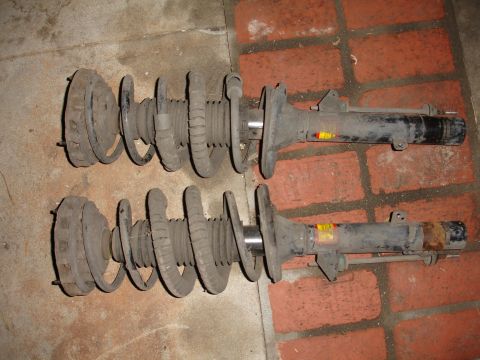 1995 Ford Taurus - Two used shock absorbers with coil springs are shown, resting on a brick and concrete floor.