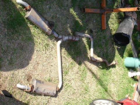 1992 Ford Taurus - A disassembled exhaust system, two mufflers and extensive piping, lies on a grassy surface.