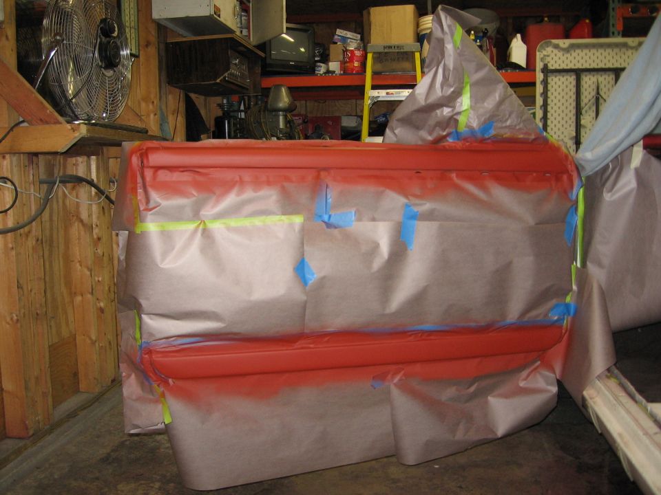Red car door covered in masking paper and tape, ready for painting
