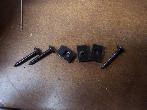 1995 Ford Probe - A collection of black screws and U-nuts are laid out on a brown, textured surface, likely for automotive use.