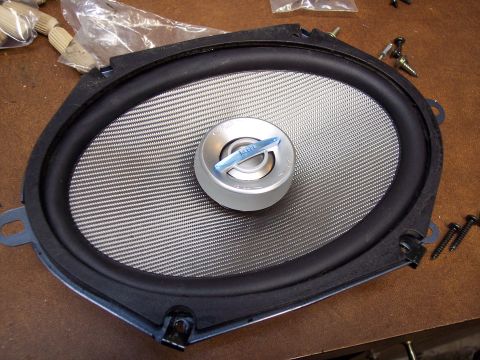 1995 Ford Probe - A car speaker is shown close-up, with a textured cone and a central tweeter. Some screws are scattered around the part.