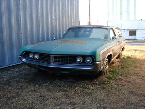 1972 Ford Ranchero - A teal 1970 Ford Torino with wood paneling and a camper shell sits parked next to a corrugated metal building.