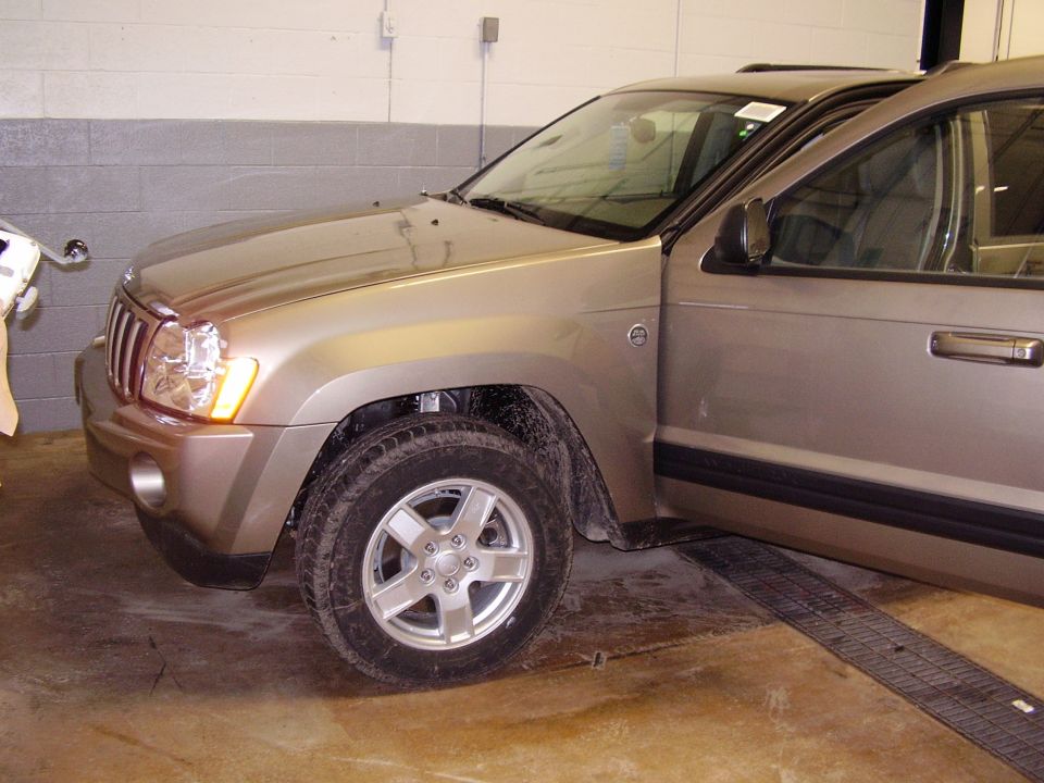 Gold Jeep Grand Cherokee parked inside with driver door open. Front wheel and fender visible