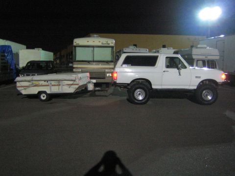 1990 Ford Bronco - A white 1990 Ford Bronco tows a pop-up trailer in a parking lot at night.