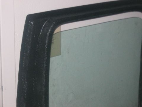 1991 Ford Bronco - Close-up of a vehicle's interior door frame and window, showing a textured black finish and a yellow sticker on the glass.