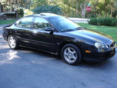 1998 Ford Taurus - A black sedan with a sunroof is parked on an asphalt driveway in front of a house and trees.