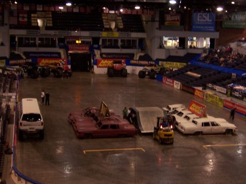 1995 Nissan Frontier - Arena event with monster trucks and vehicles prepared for stunts, including a ramp and a forklift.