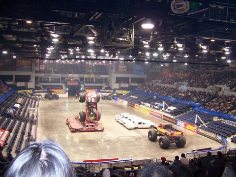 1995 Nissan Frontier - Monster trucks perform in an arena with spectators in the stands.
