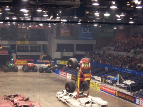 1995 Nissan Frontier - Monster trucks compete in an indoor arena event with spectators in the stands.