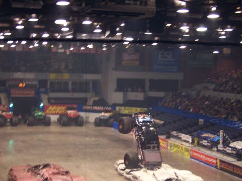 1995 Nissan Frontier - A monster truck is captured mid-air, balancing on its rear wheels during a performance in an arena with spectators.