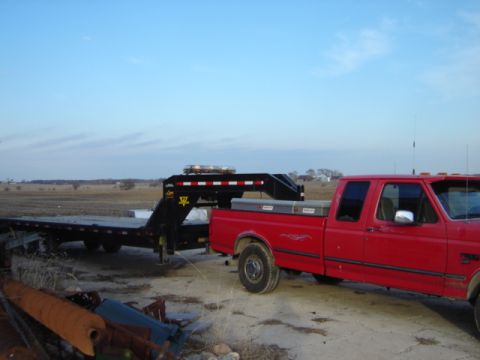 1992 Ford Bronco - A red pickup truck is hitched to a large gooseneck trailer, parked outdoors under a clear sky.