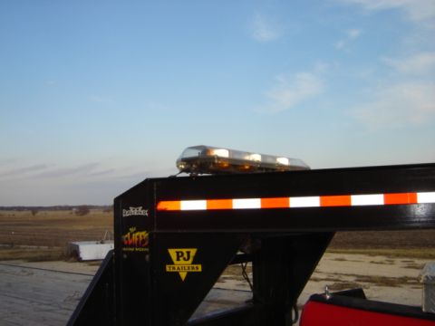1992 Ford Bronco - A gooseneck trailer is equipped with an amber light bar and reflective tape under a clear sky.